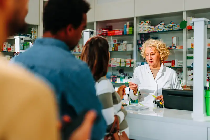 female pharmacist working behind counter of a busy pharmacy