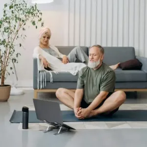 man doing yoga on the floor in front of laptop with woman on sofa