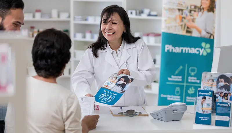 Pharmacist handing a pharmacy marketing flyer to customer with their prescription