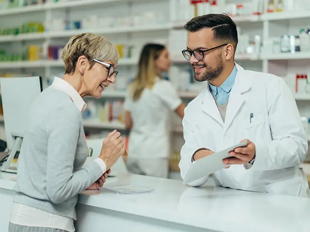 Young male pharmacist giving prescription medications to senior female customer in a pharmacy