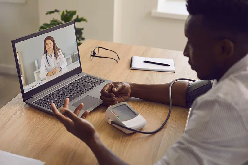 Sick man with hypertension measures high blood pressure using sphygmomanometer during webcam telemedicine teleconference with online doctor