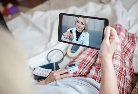 Old woman in bed looking at screen of laptop and consulting with a doctor online at home rpm category